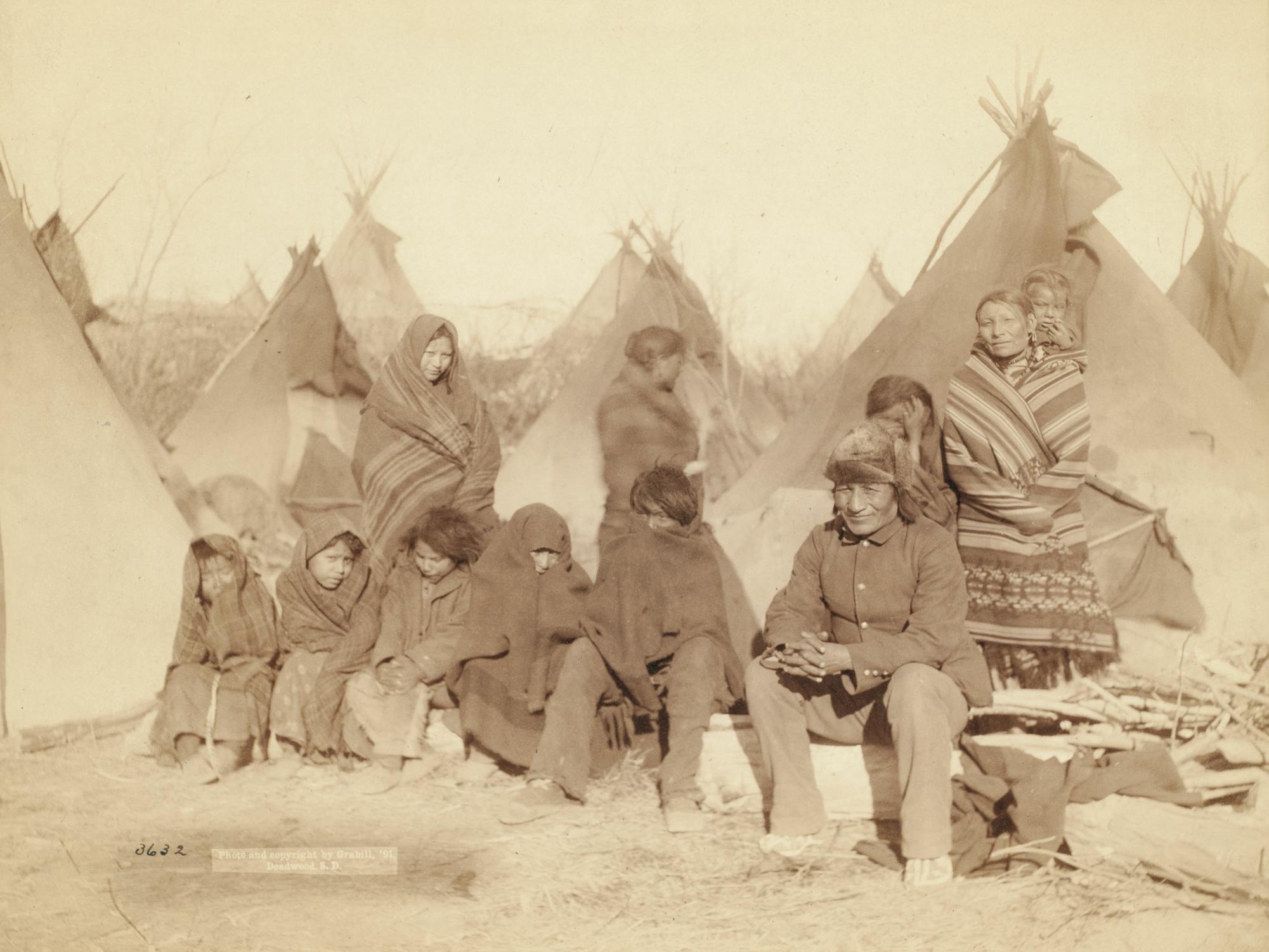 Group of eleven Miniconjou (children and adults) in a tipi camp, probably on or near Pine Ridge Reservation.